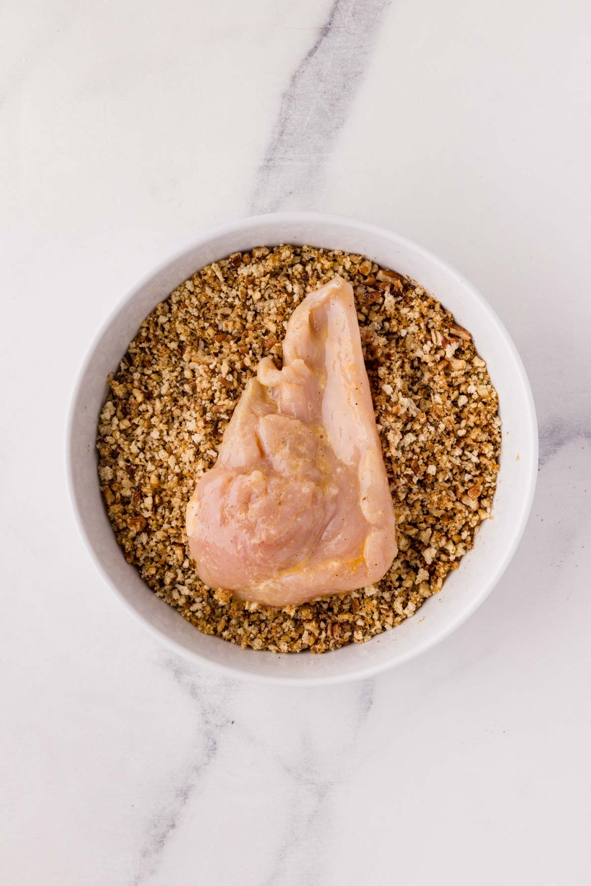 Dipping a chicken breast into the pecan breading in a bowl.