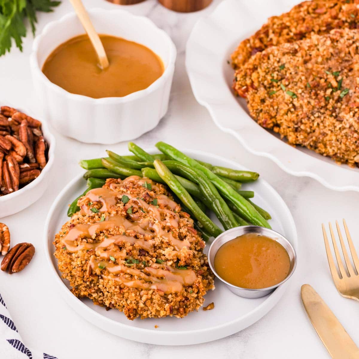 Pecan crusted chicken on a plate with sauce and green beans on the side.