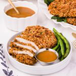 Sliced pecan crusted chicken on a plate with green beans and sauce.