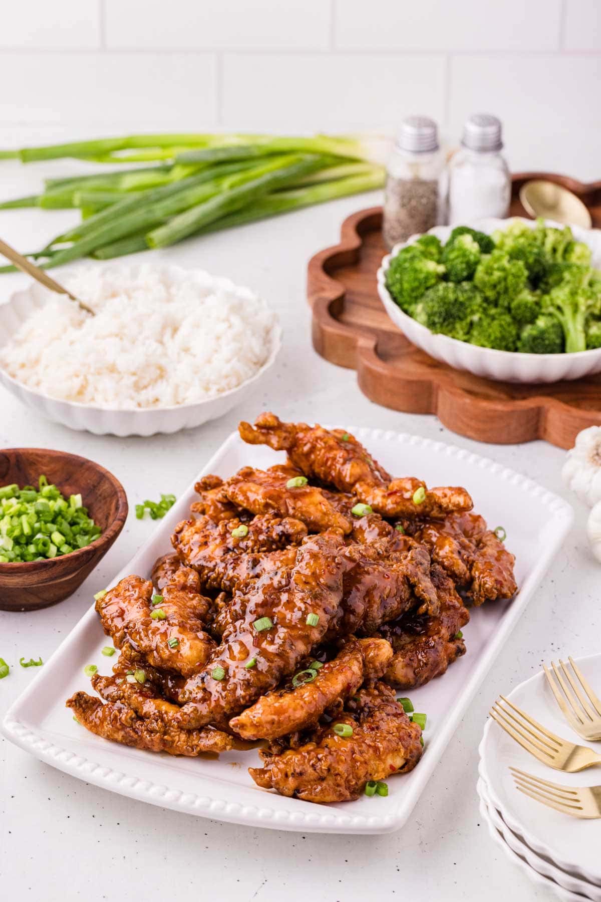 Sweet chili chicken fingers on a serving platter next to a bowl of rice and broccoli.