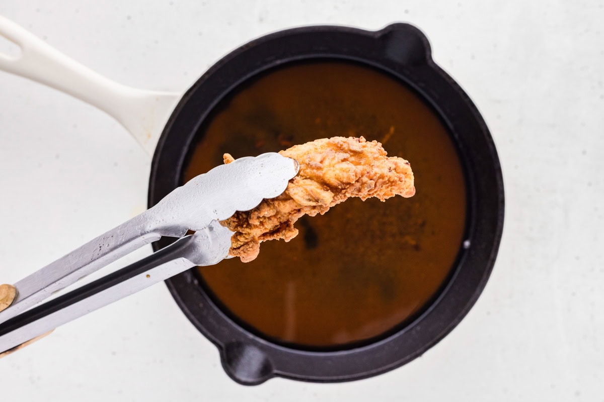 Using a tong to pick up a fried chicken tender from oil.