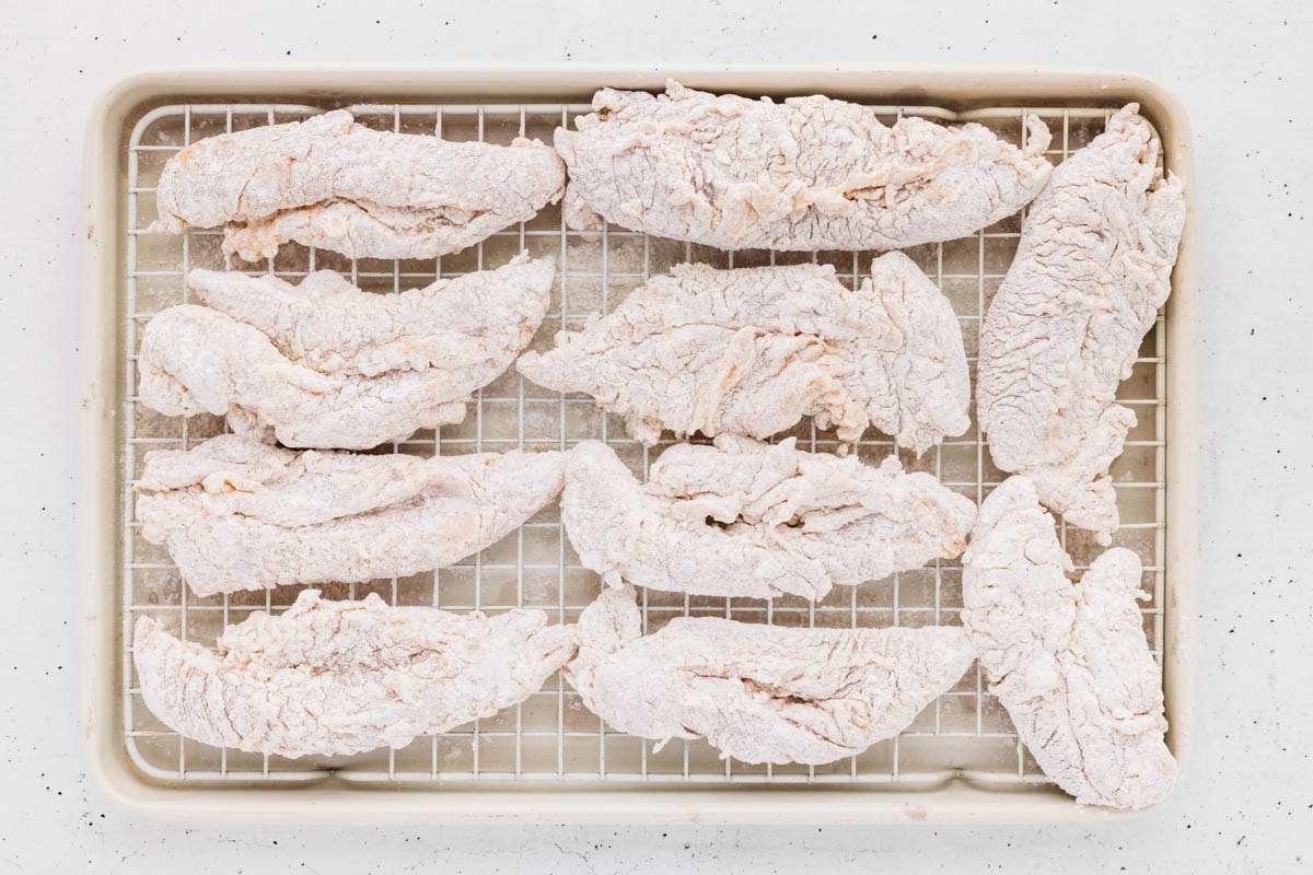 Breaded chicken tenders on a baking sheet lined with a wire rack.