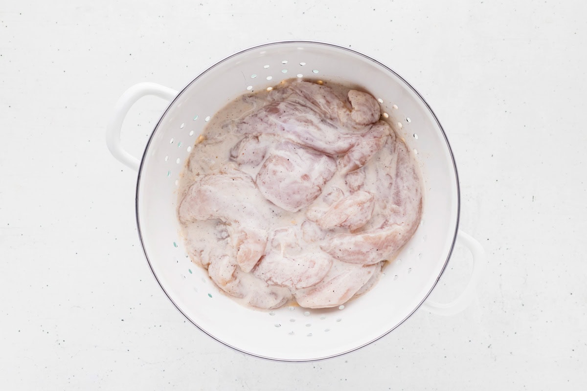 Chicken and buttermilk marinade in a colander.