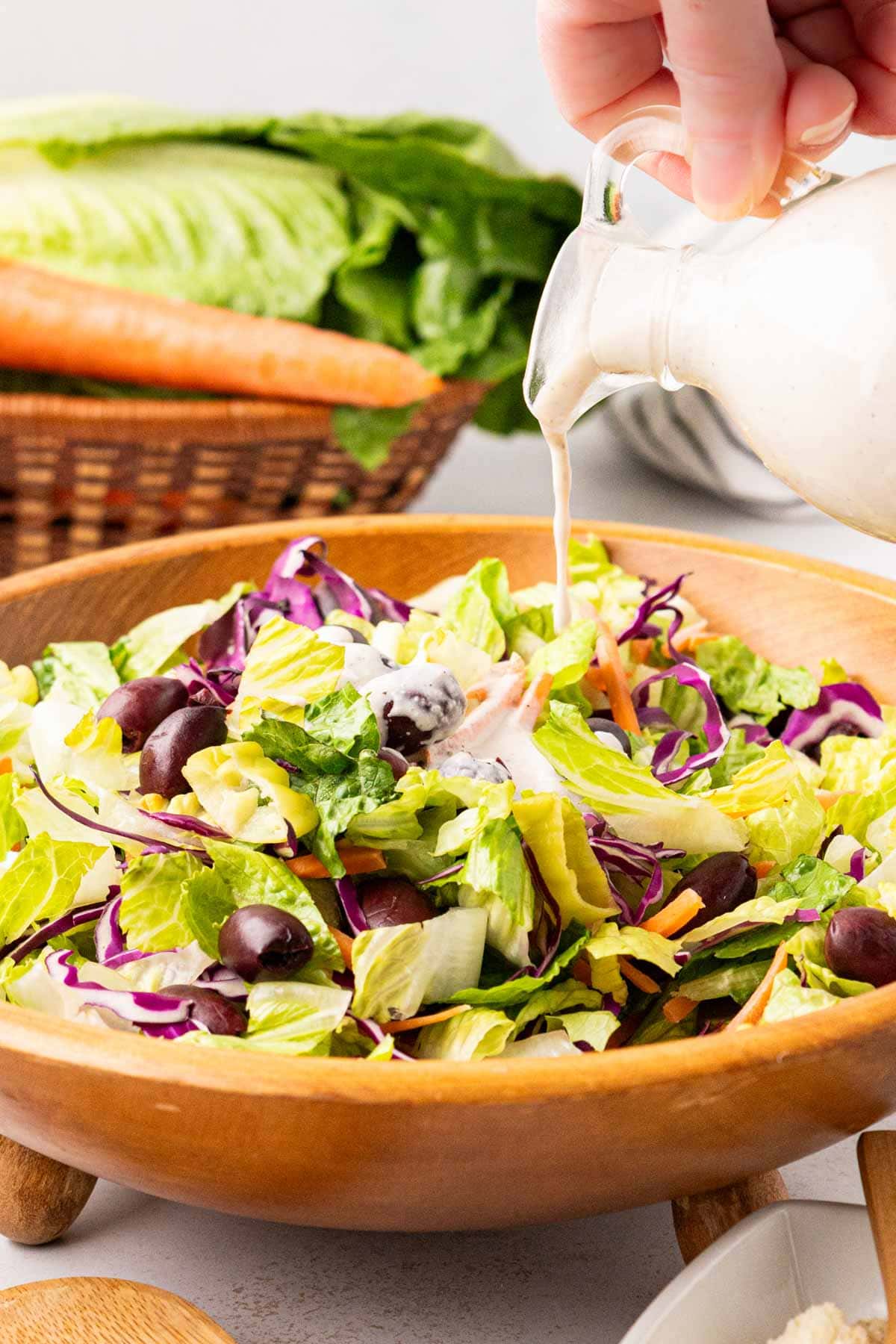 Pouring creamy parmesan salad dressing on an Italian house salad.