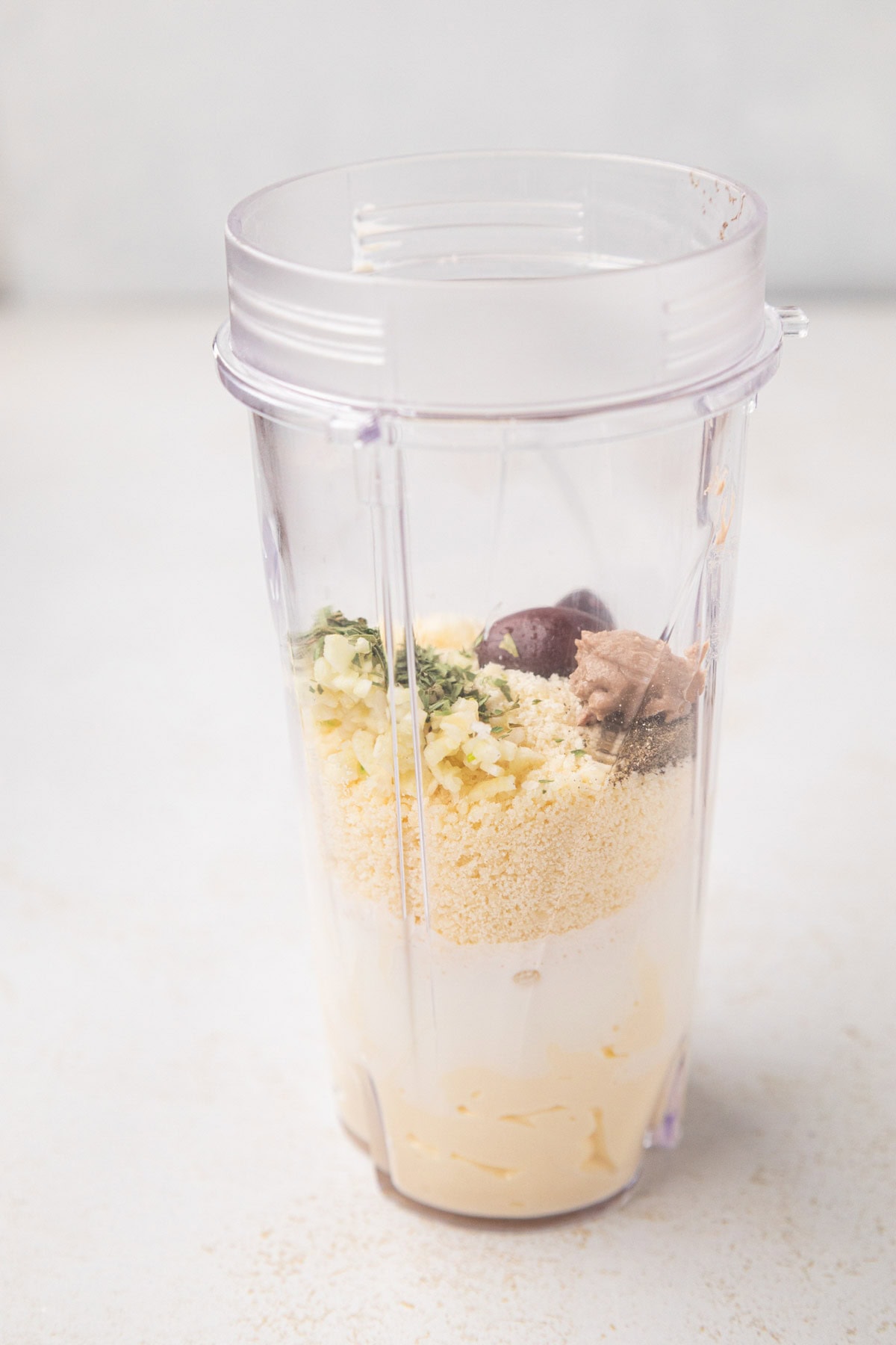 A side view of the blender cup with ingredients for the creamy parmesan salad dressing.