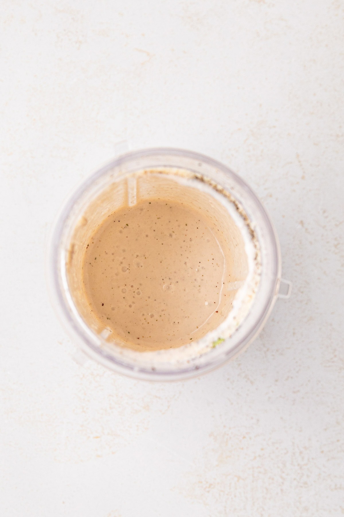 An overhead view of the blender cup with the blended creamy parmesan salad dressing.