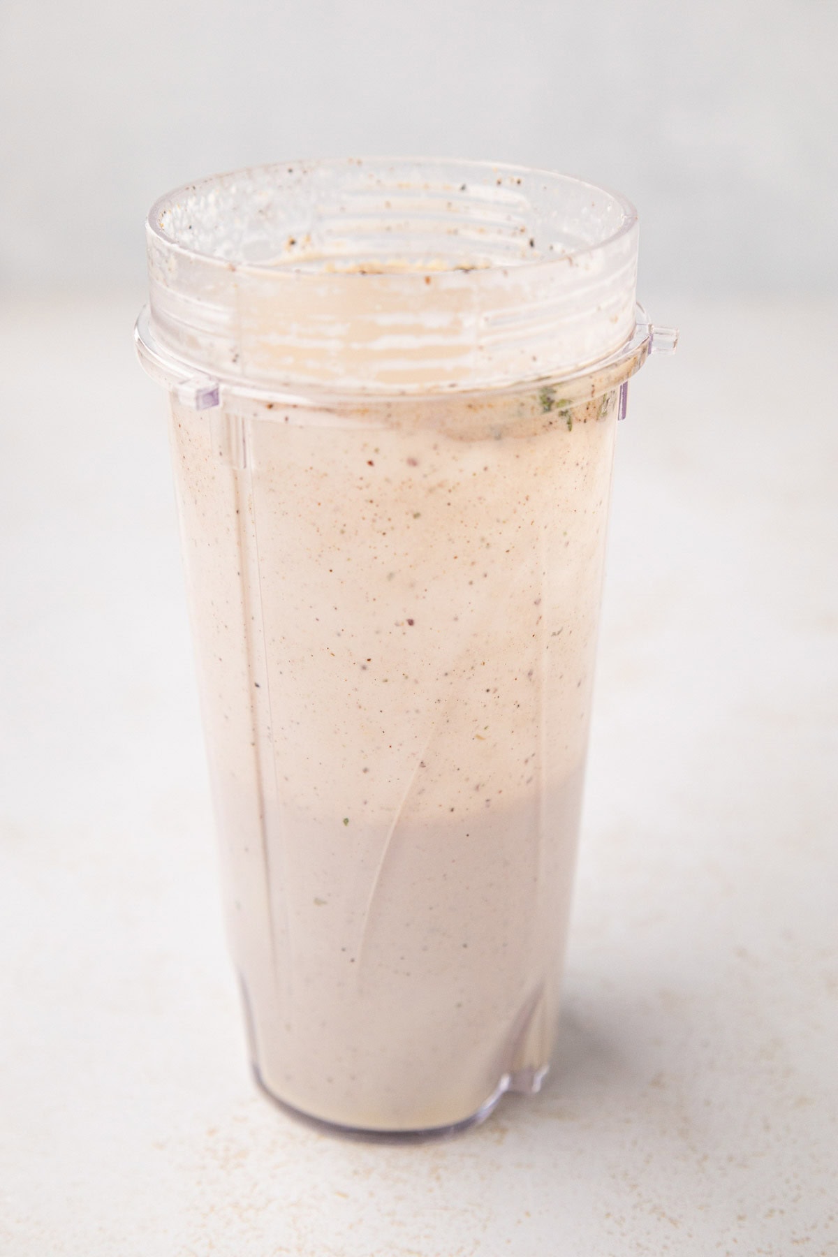 A side view of the blender cup with the blended creamy parmesan salad dressing.