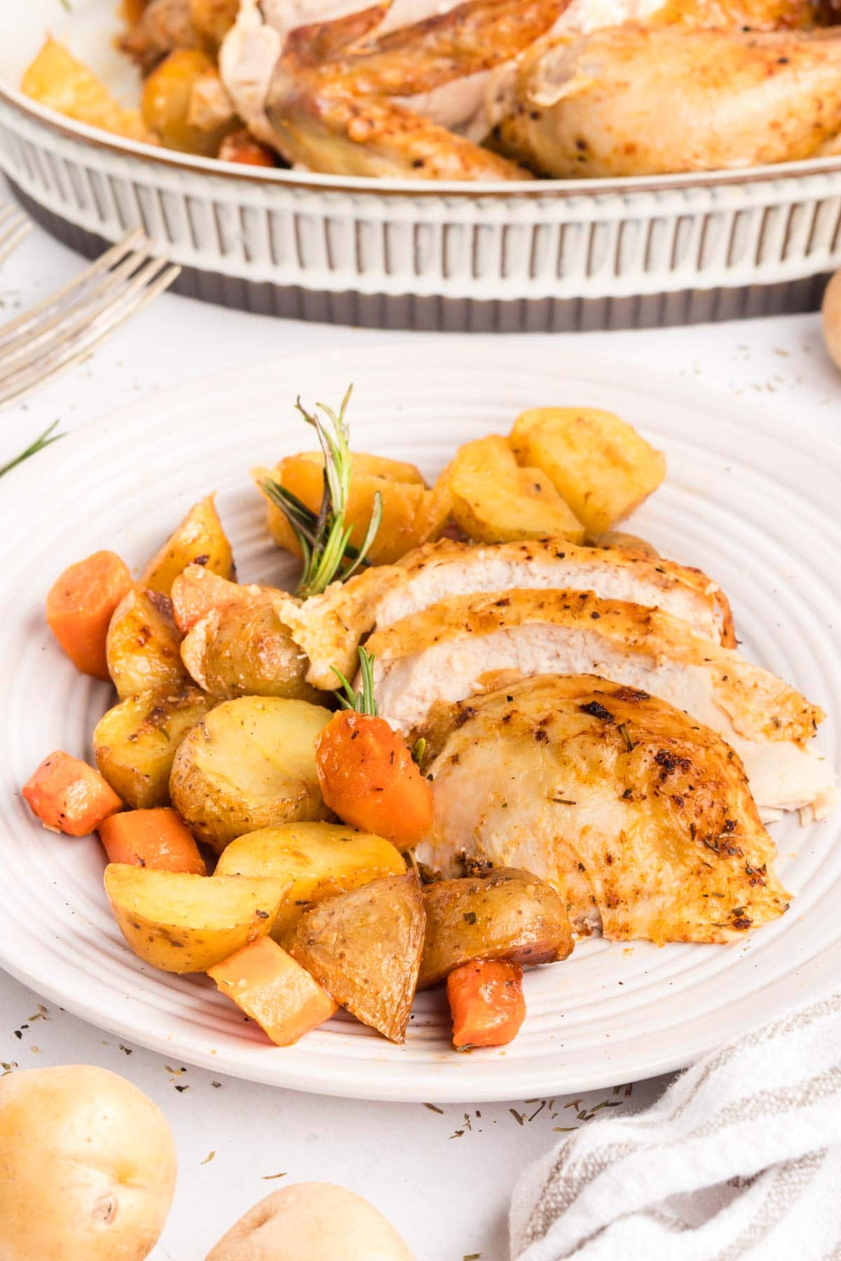 Sliced roasted chicken served on a plate with a side of potatoes and carrots.