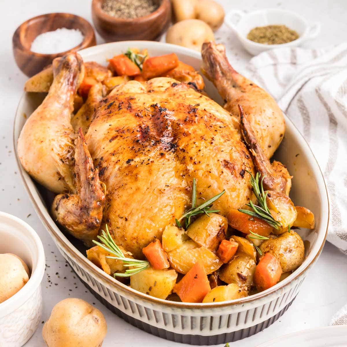 Whole roasted chicken served on a bed of carrots and potatoes in a serving dish.