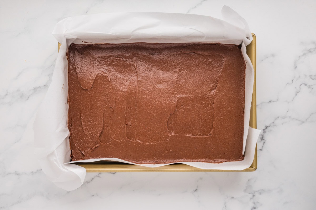 Brownie batter placed in a parchment lined baking pan.
