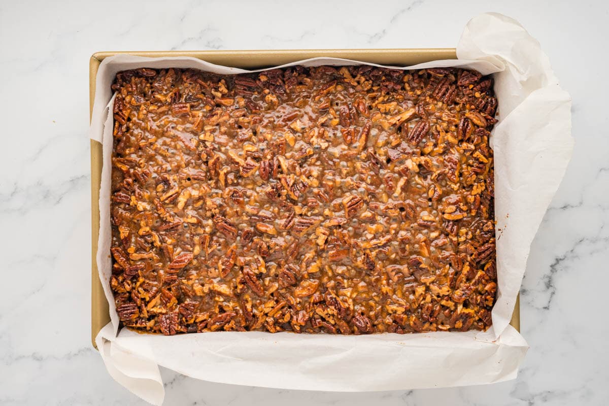 Baked pecan pie brownies in a parchment lined baking dish.