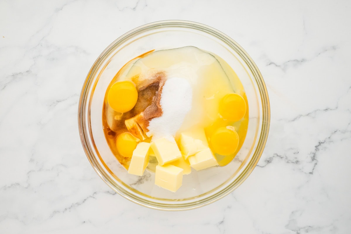 Sugar, eggs, butter, and vanilla in a mixing bowl before being combined.