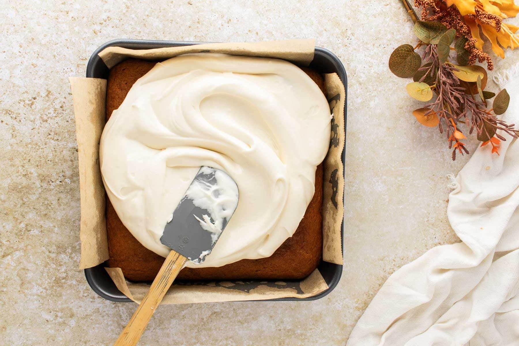 Spreading the cream cheese frosting on top of pumpkin bars in a baking dish.