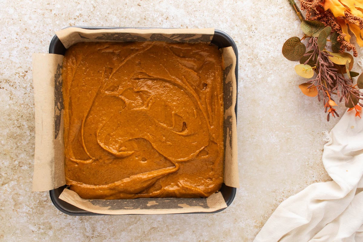 Pumpkin bars batter spread in a parchment lined baking pan.