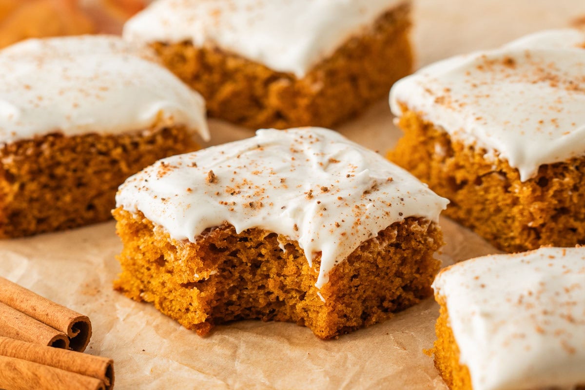 Pumpkin bars with cream cheese frosting with one missing a bite.