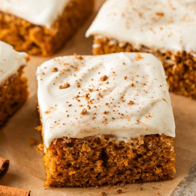 Close up of a pumpkin bar with cream cheese frosting with more bars behind it.