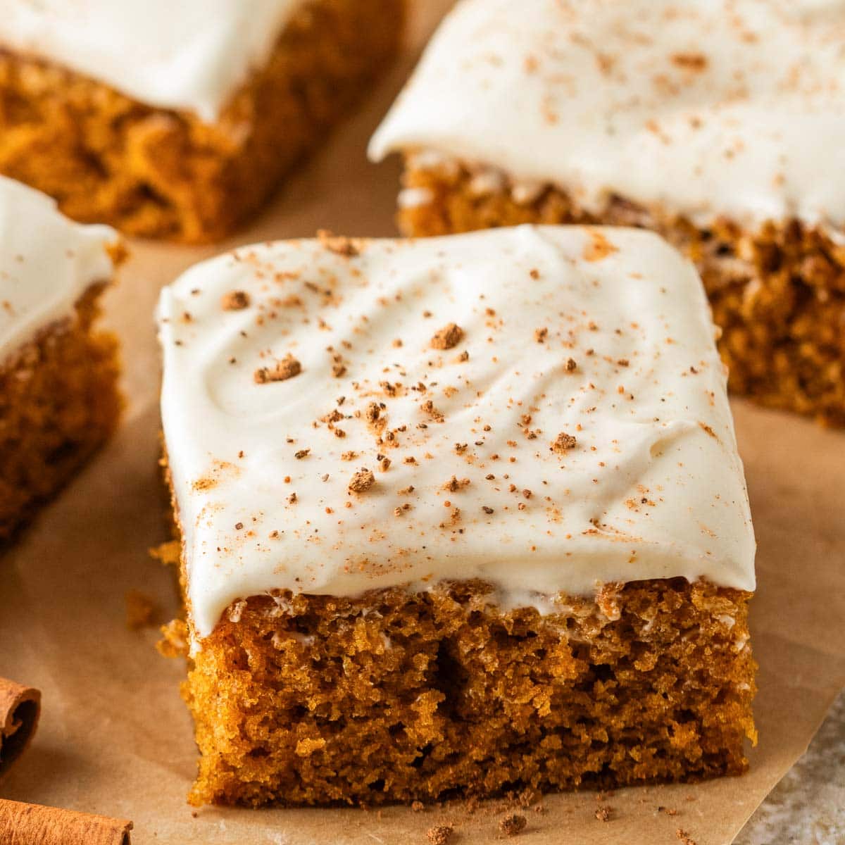 Close up of a pumpkin bar with cream cheese frosting with more bars behind it.