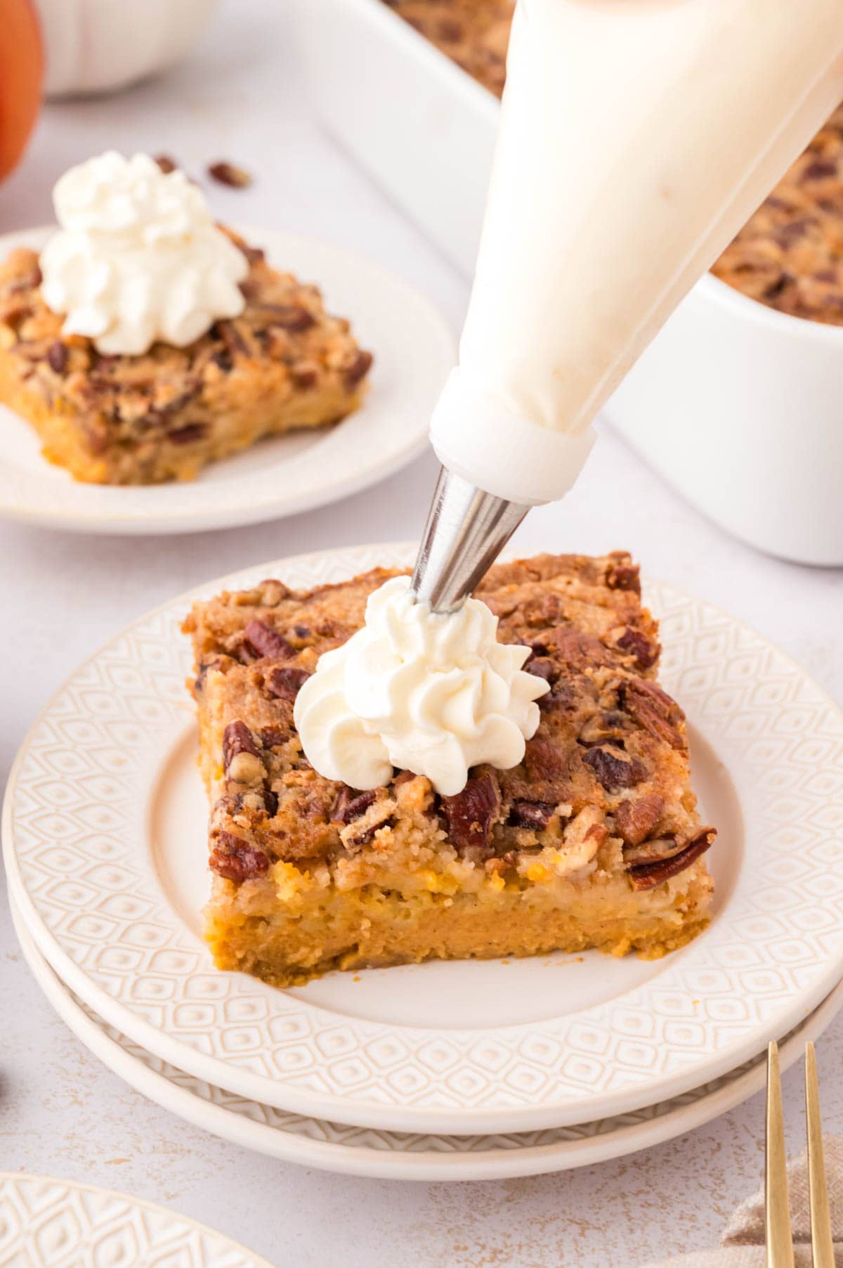Piping whipped cream onto a slice of pumpkin crunch cake.