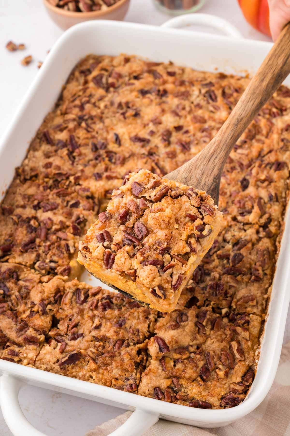 Removing a slice of pumpkin dump cake with a wooden spatula.