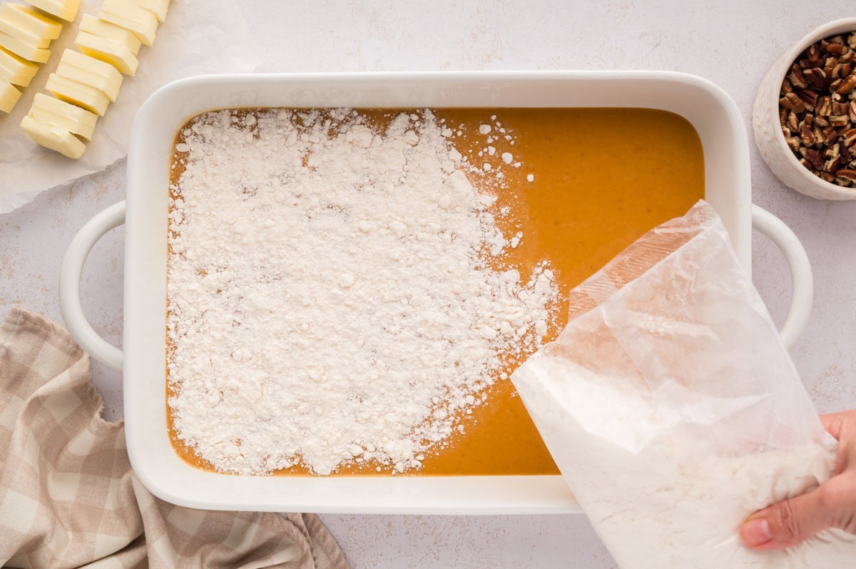 Sprinkling the cake mix from the bag onto the top of the pumpkin custard layer in the baking dish.