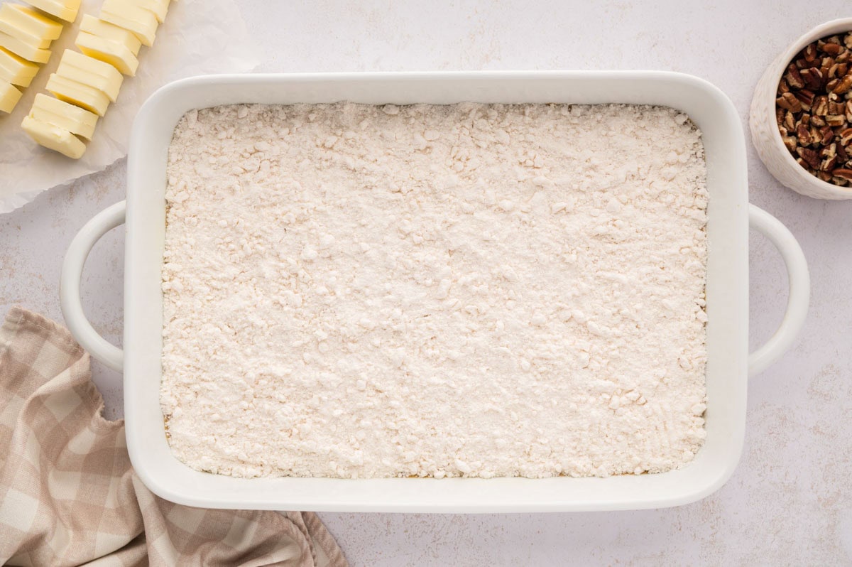The cake mix evenly covering the pumpkin custard layer in the baking dish.