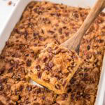 Removing a slice of pumpkin dump cake with a wooden spatula.