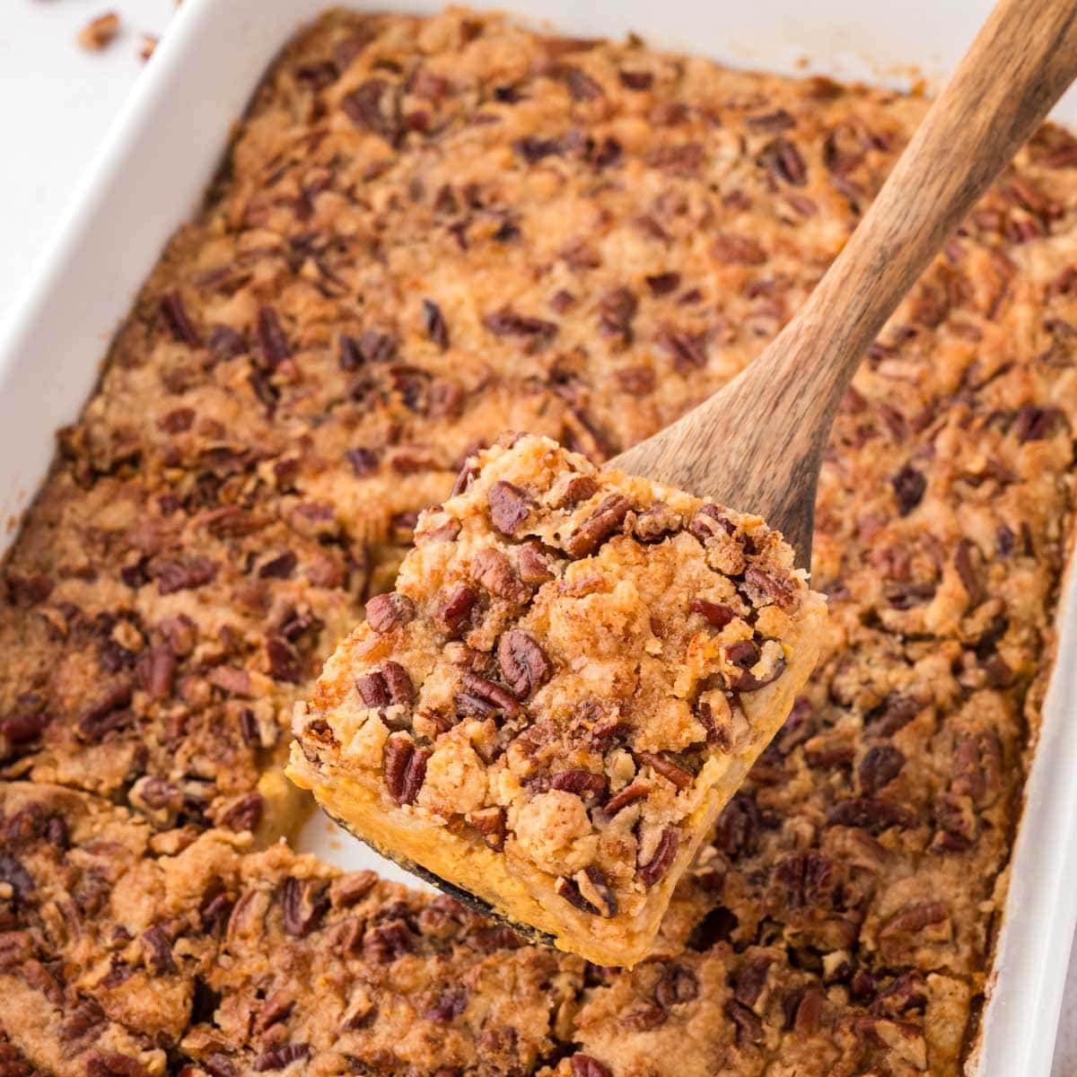 Removing a slice of pumpkin dump cake with a wooden spatula.