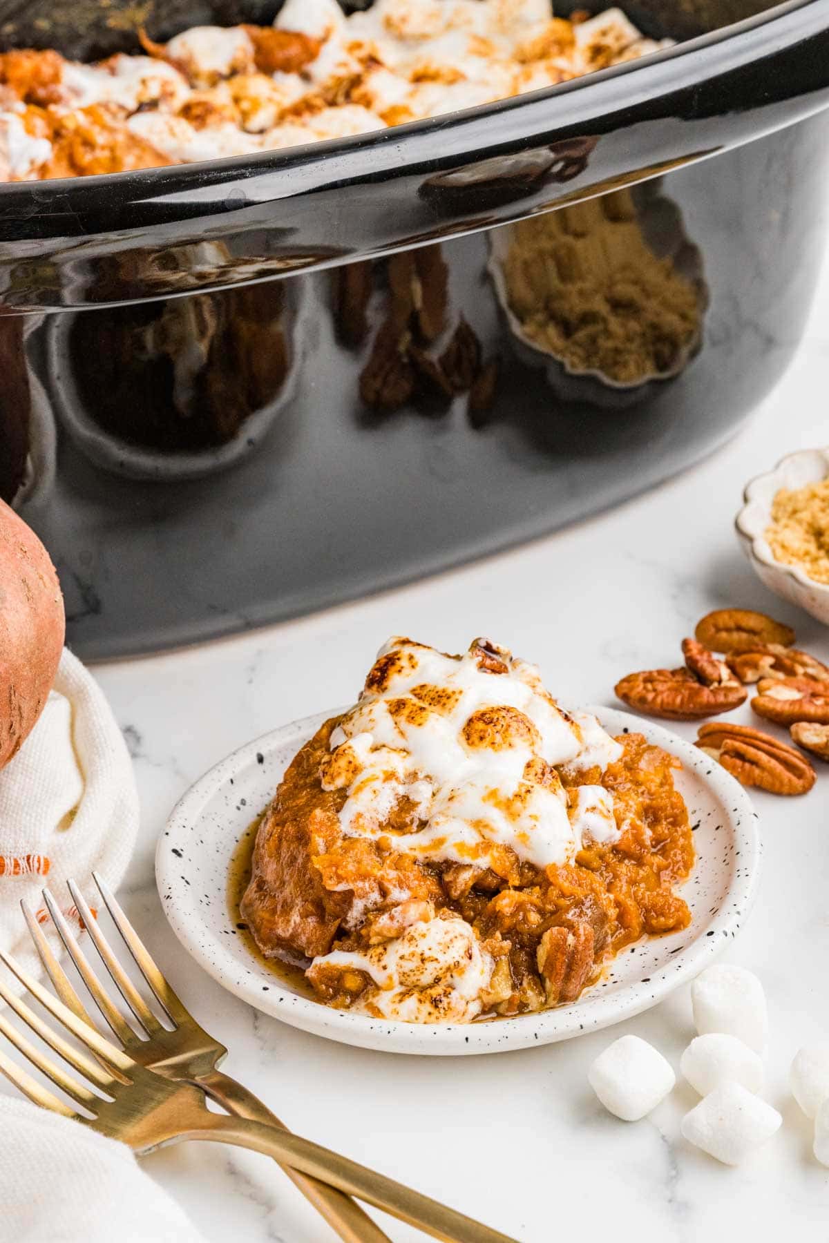 Portion of sweet potato casserole on a plate with more in a crockpot behind it.