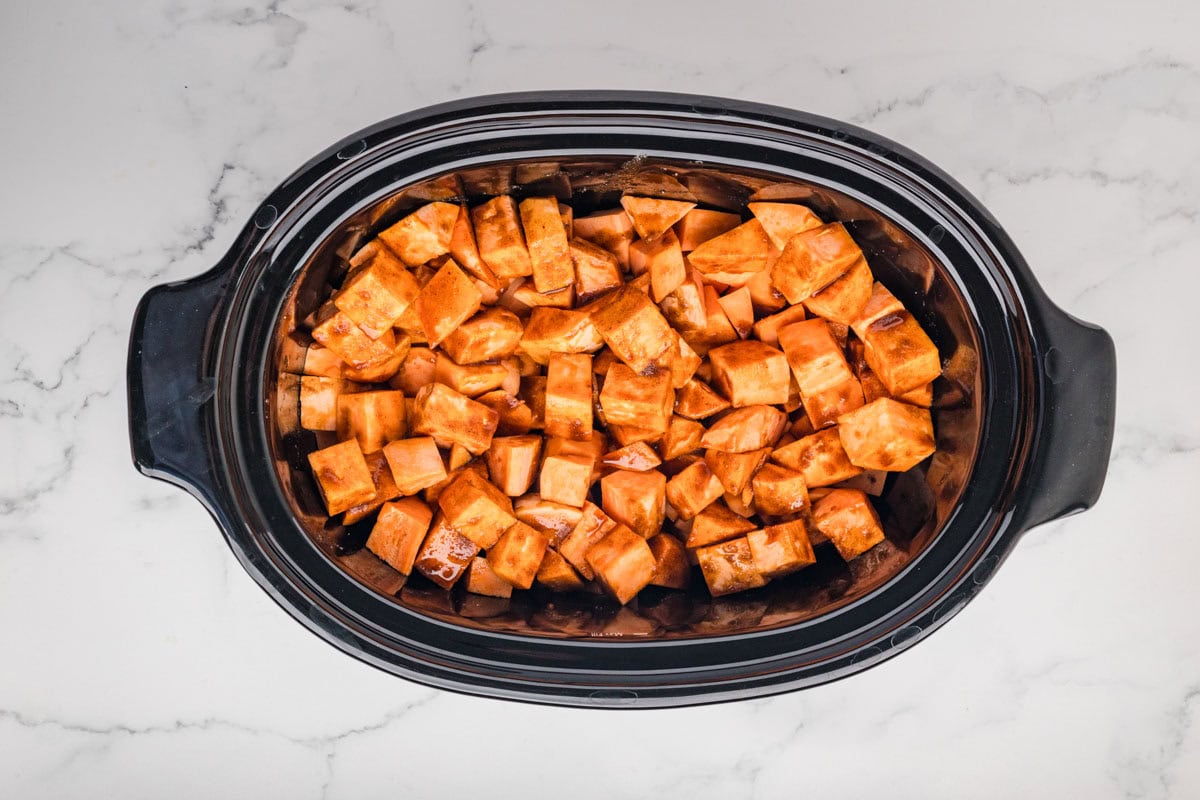 Diced sweet potatoes mixed with sugar and butter mixture in a slow cooker.