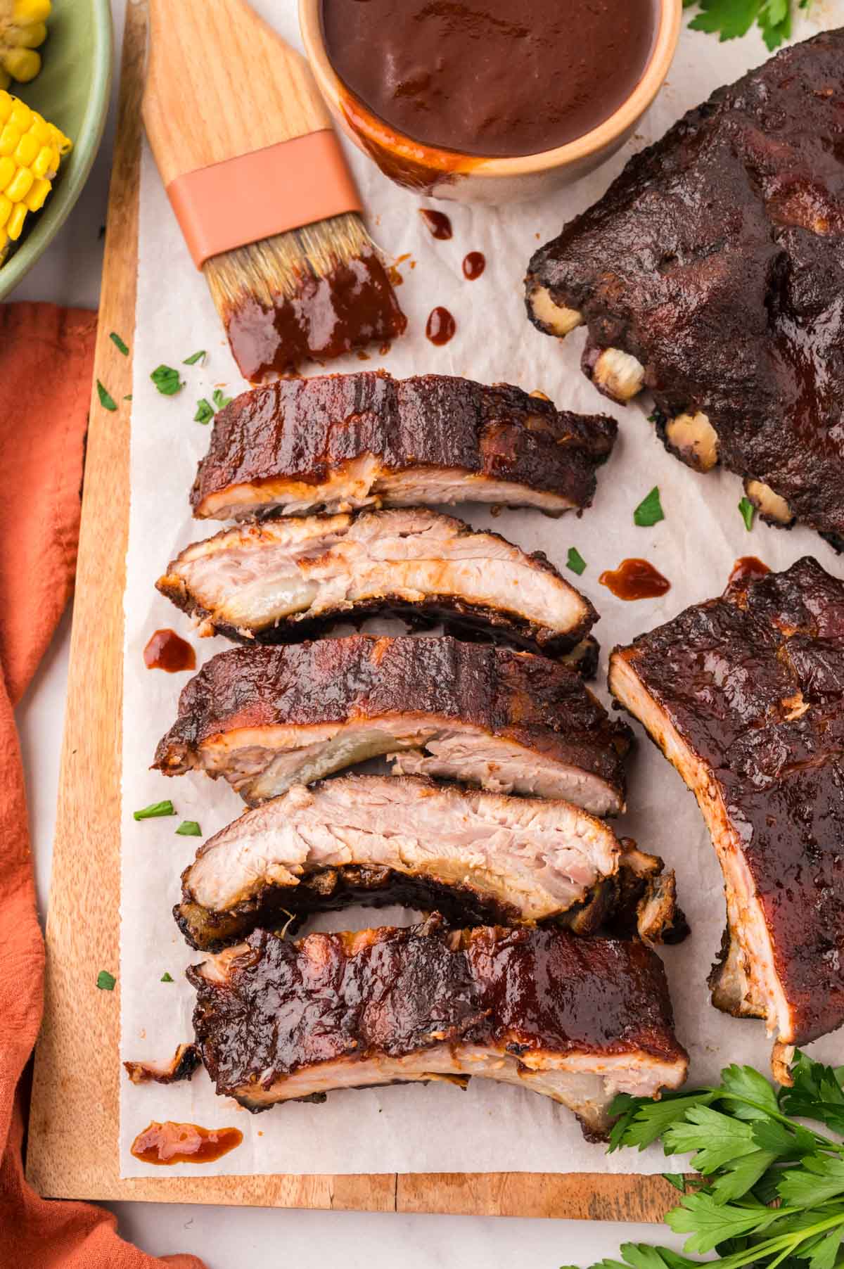 Sliced smoked baby back ribs on a wooden tray with serving bowl of bbq sauce on the side.