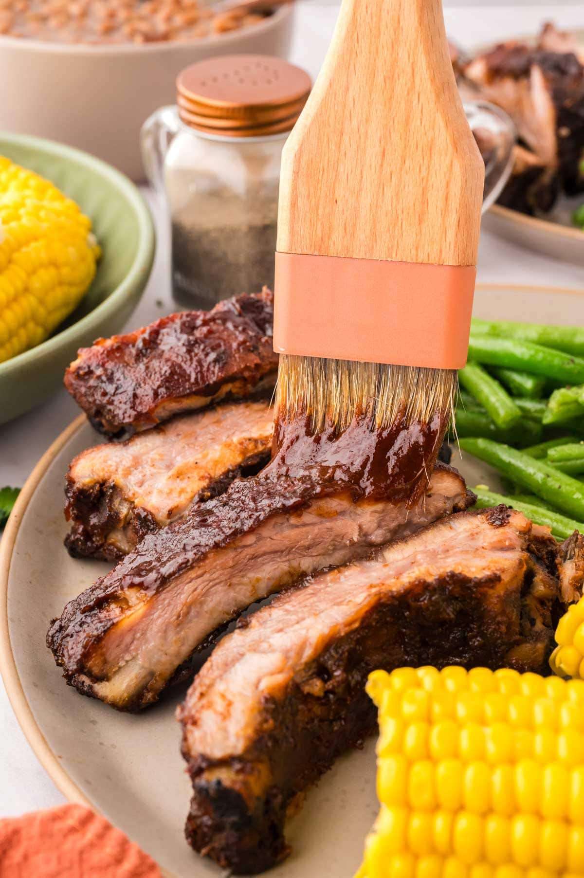 Slice smoked baby back ribs on a plate with corn and green beans.