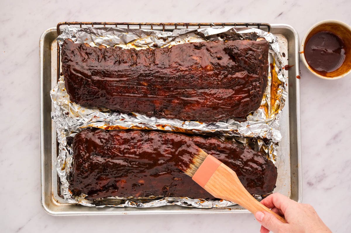 Brushing barbecue sauce on racks of ribs.