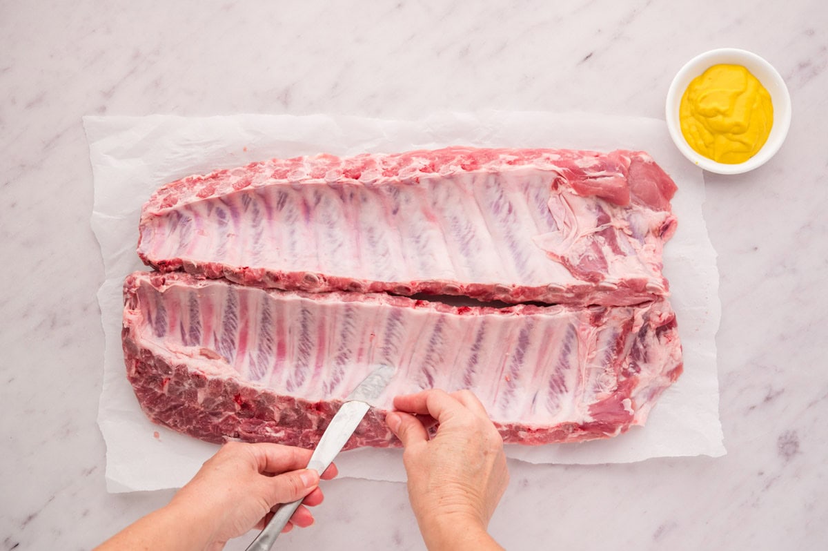 Slipping a knife under the membrane of pork ribs to lift it.