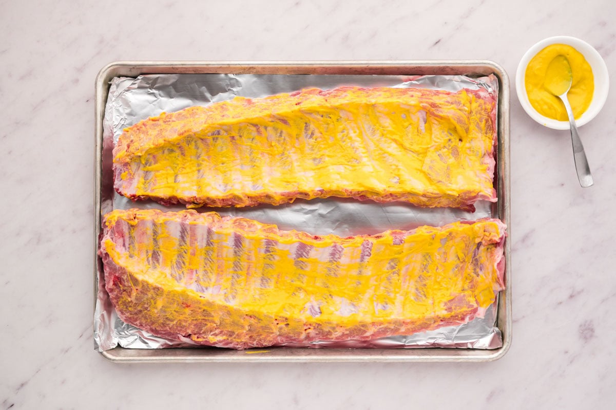 Back side of baby back ribs lightly coated with yellow mustard.