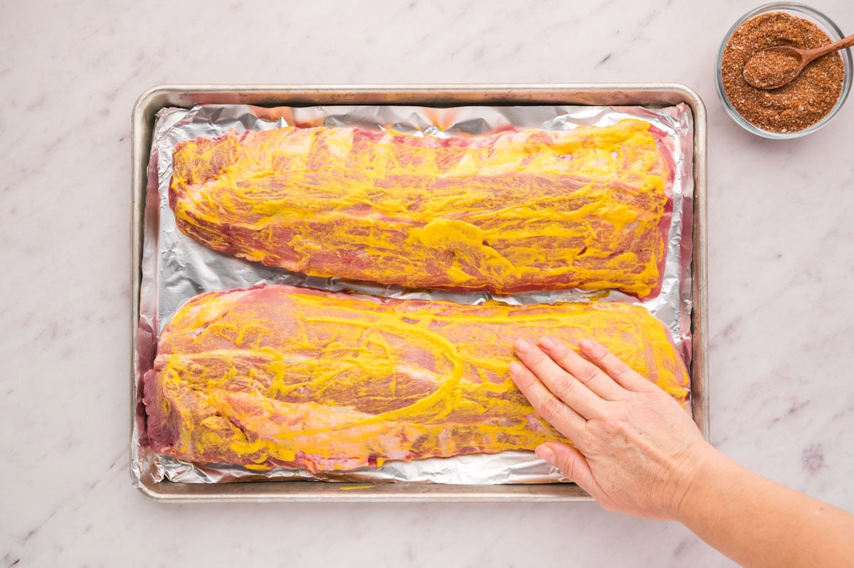 Meaty side of baby back ribs lightly coated with yellow mustard.