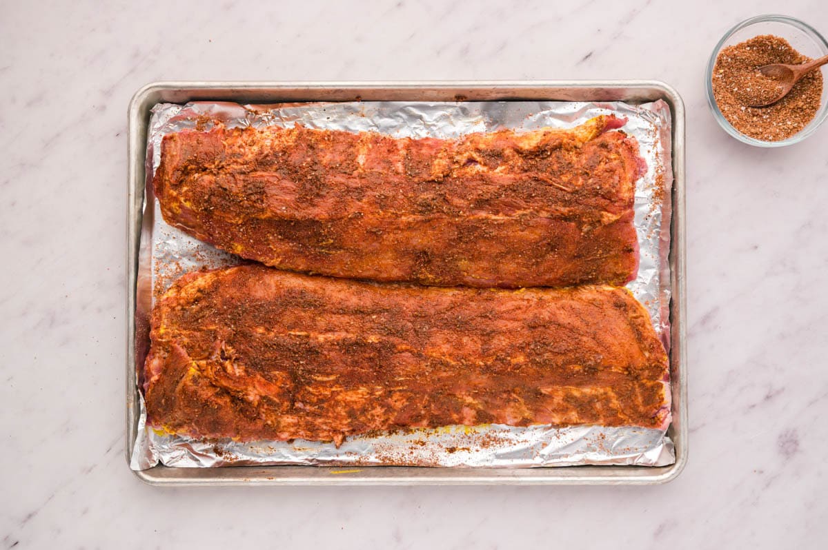 Rb rub seasoning coated all over both racks of ribs on a lined baking pan.