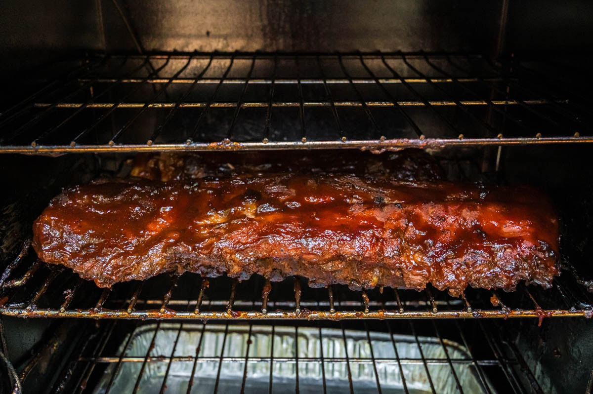 Baby back ribs with bbq sauce caramelized on them in a smoker.