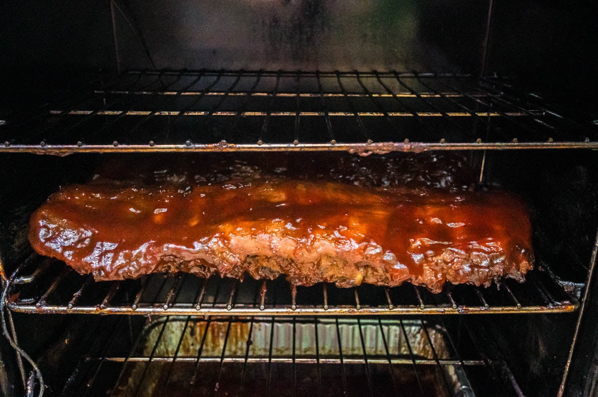 Baby back ribs with bbq sauce on them in a smoker.