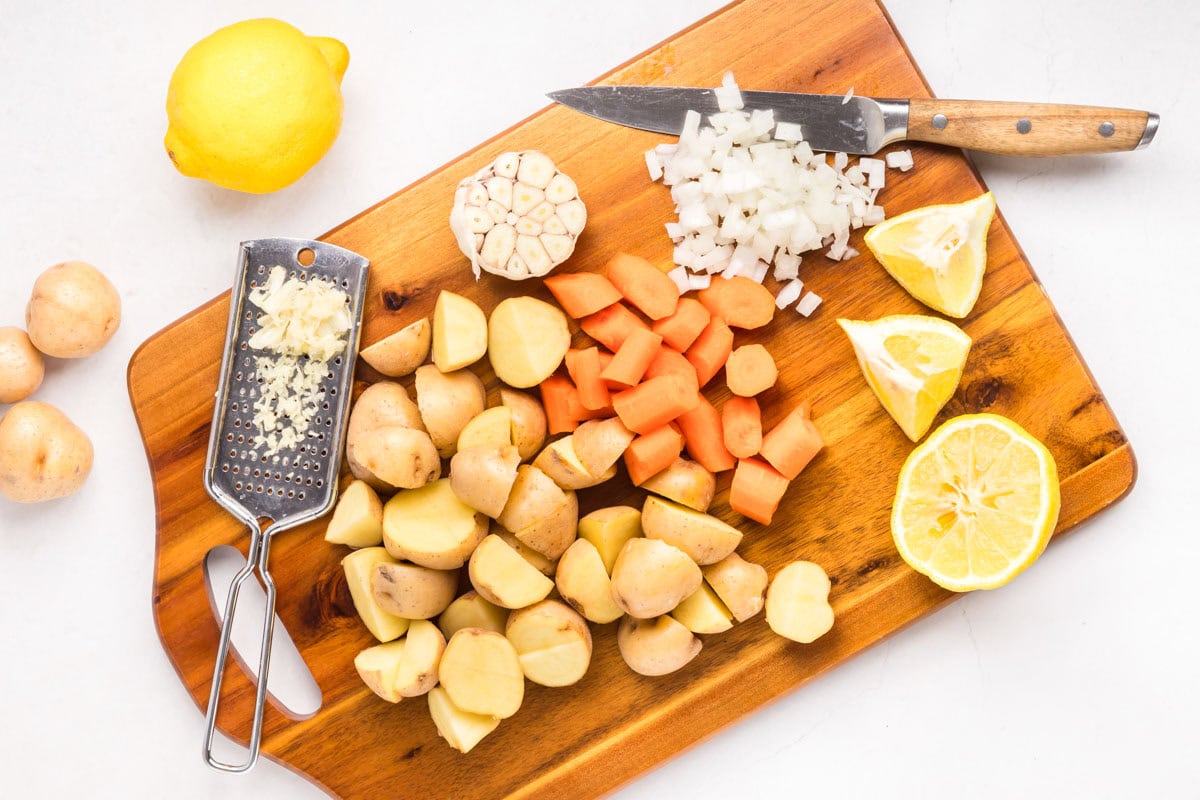 Chopping lemons, potatoes, carrots and onions on a wooden chopping board.