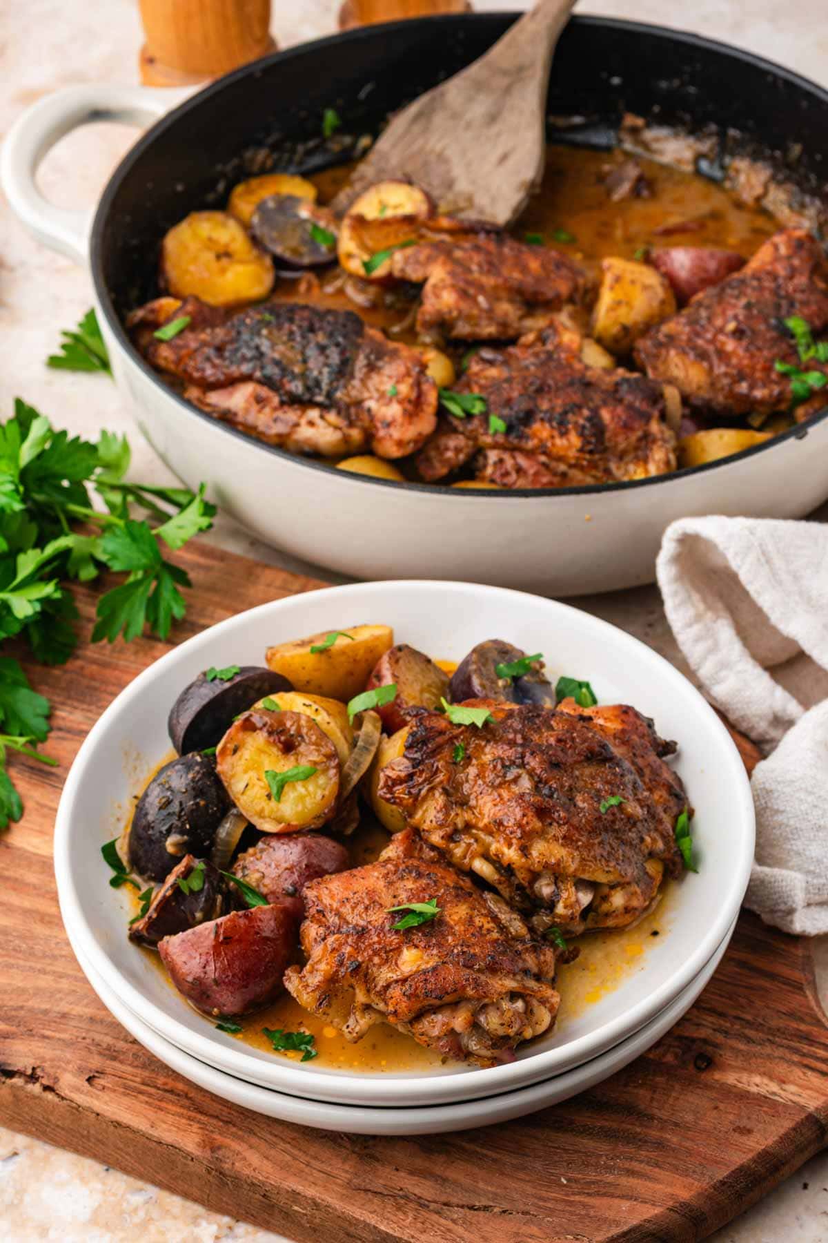 Braised maple dijon chicken thighs served on a plate with more in a skillet in the background.