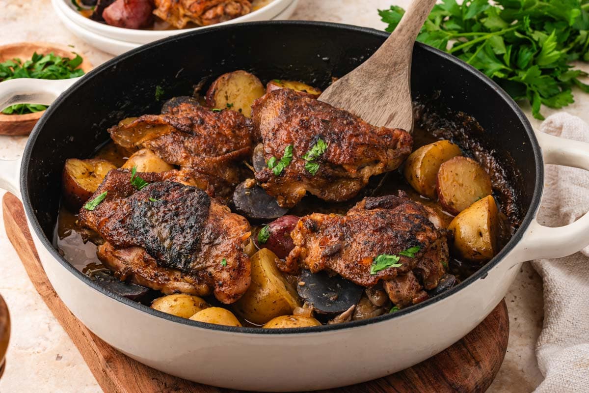 Maple dijon chicken thighs in a skillet with potatoes.