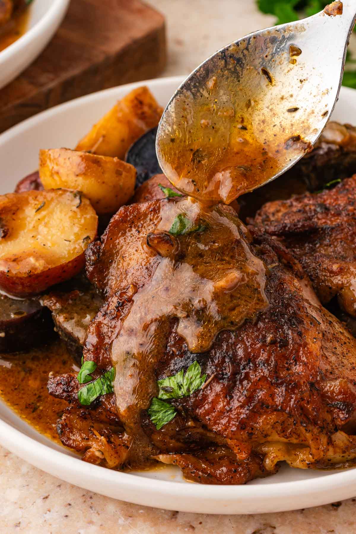 Spooning juices over the top of a maple dijon chicken thigh on a plate.