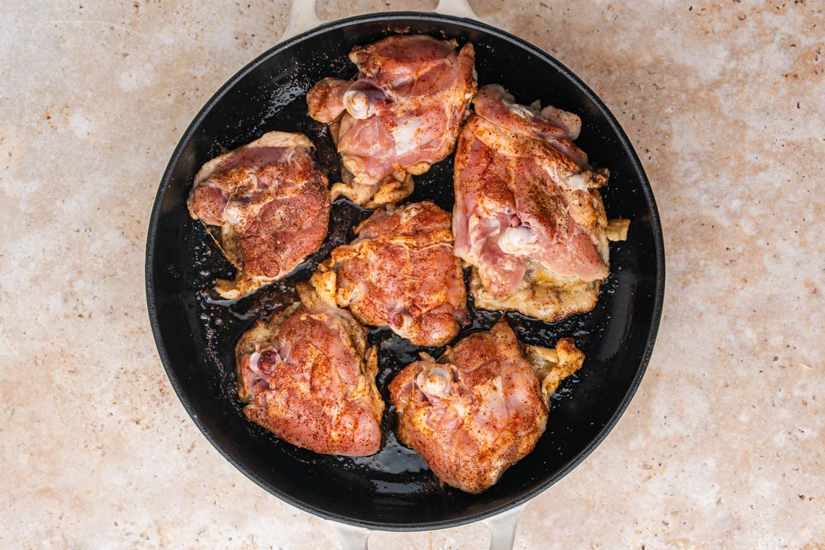 Seasoned chicken thighs in a cast iron skillet to sear.