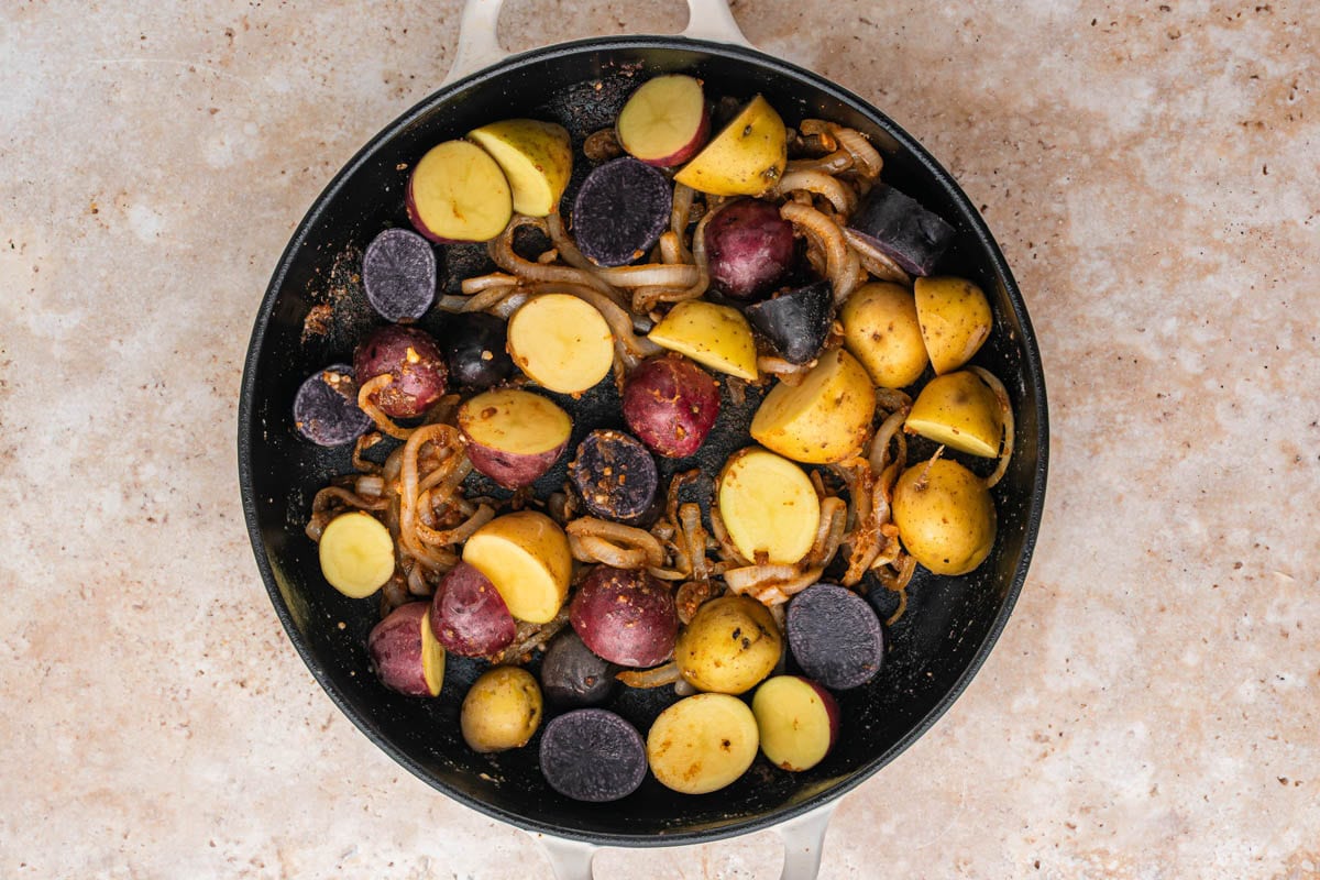 Halved baby potatoes placed in a skillet with sauteed onions.