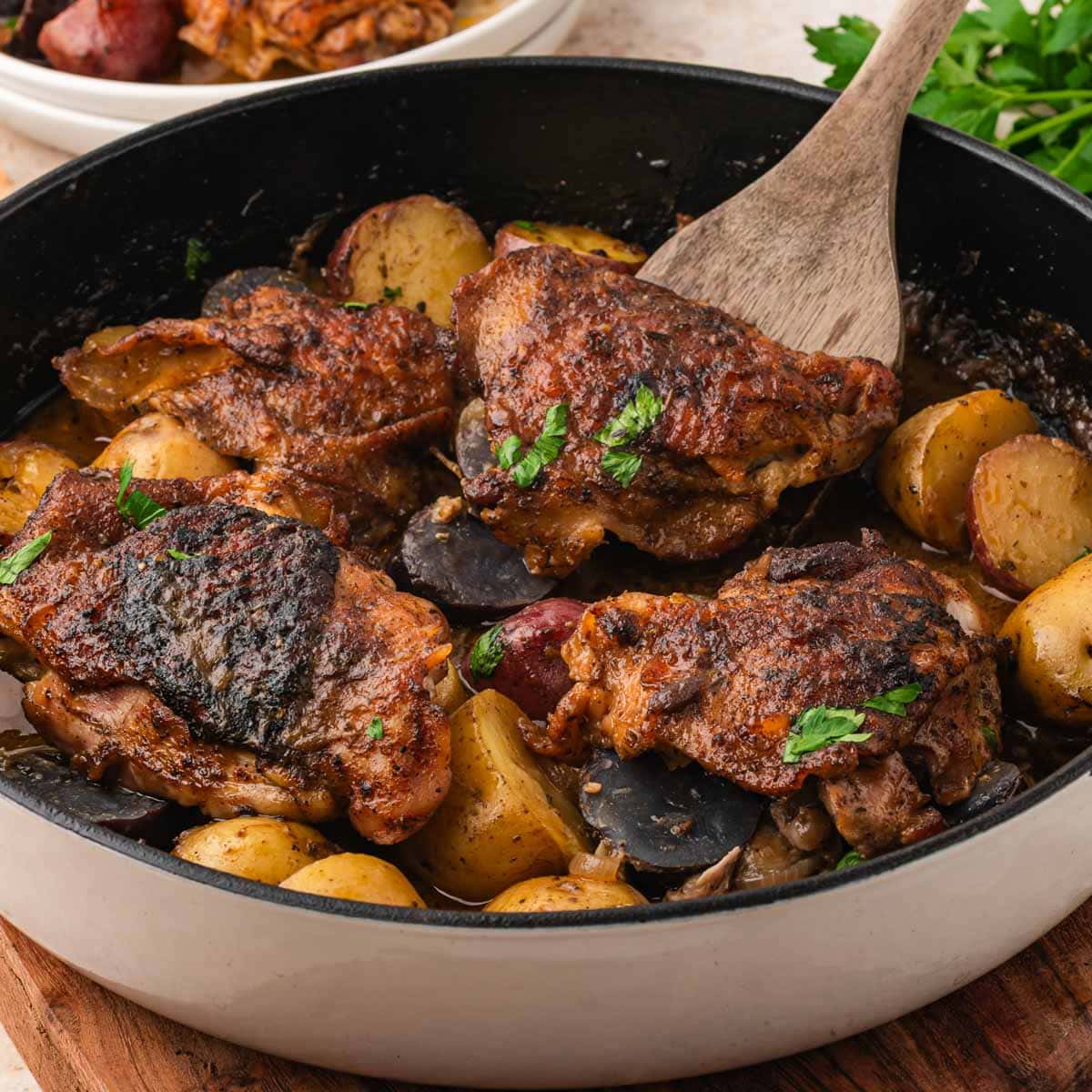Maple dijon chicken thighs in a skillet with potatoes.