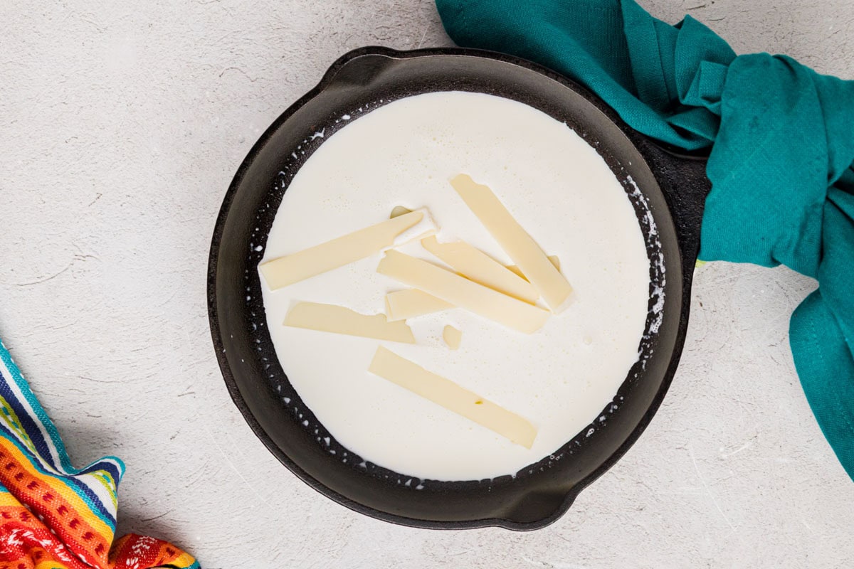 Shreds of American cheese added to the heavy cream in a saucepan.