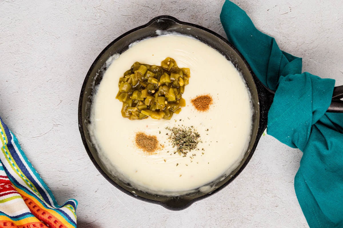 Green chiles and spices added to the queso mixture in a pan.