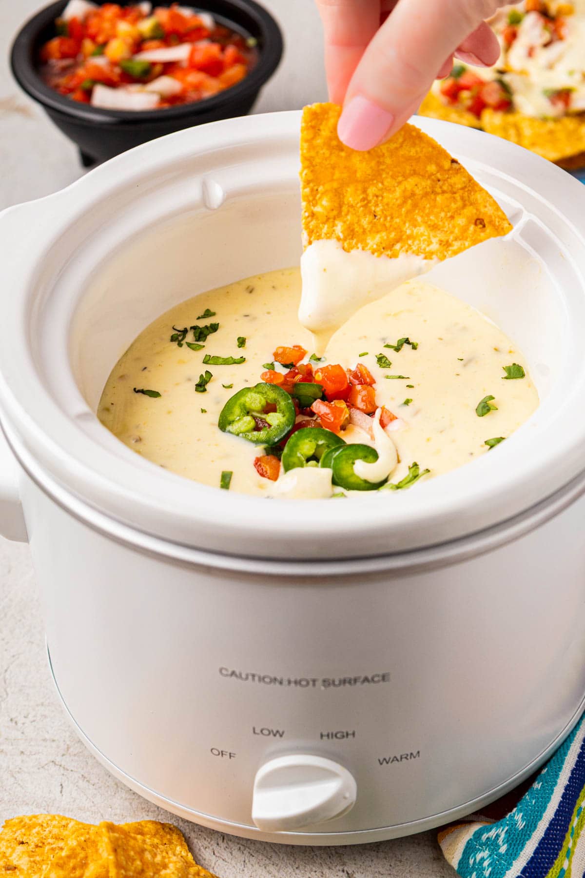 Hand dipping a chip into white queso in a small crockpot.