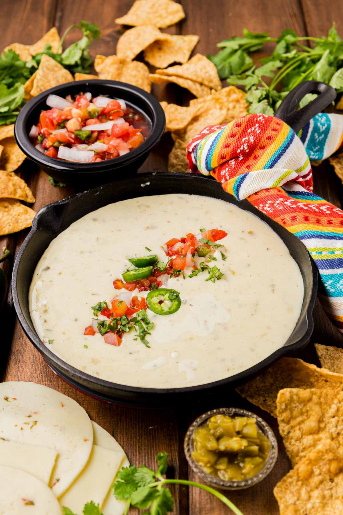 White queso dip served in a cast iron skillet with tomatoes and jalapenos on top.