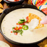Hand dipping a chip into a skillet of white queso.